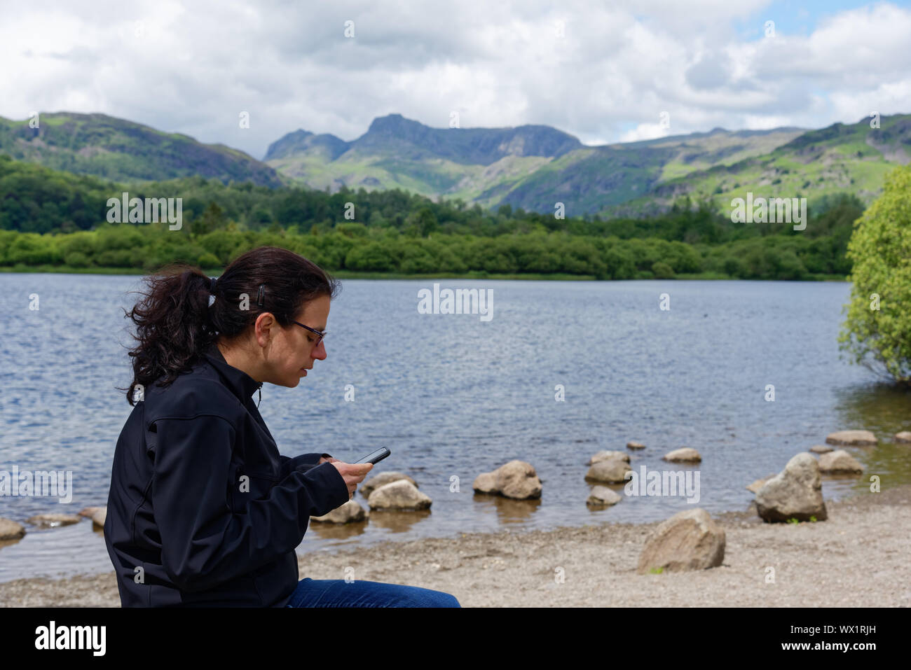 Une jeune femme en ignorant les paysages du Lake District de se concentrer sur son téléphone cellulaire, Lake Road, UK Banque D'Images