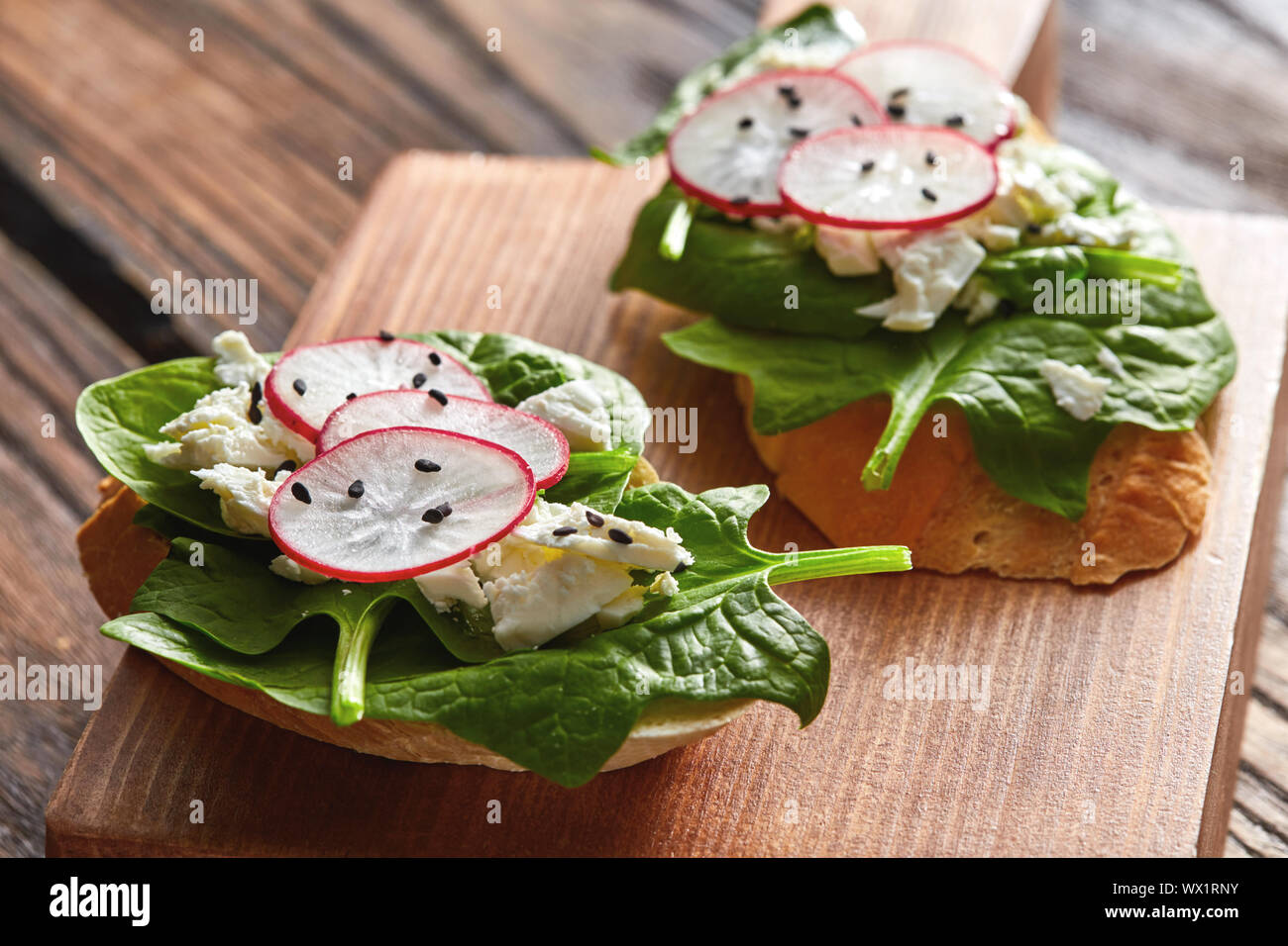 Bruschetta avec les radis, les épinards et le fromage blanc avec les graines de lin sur un fond de bois. Banque D'Images