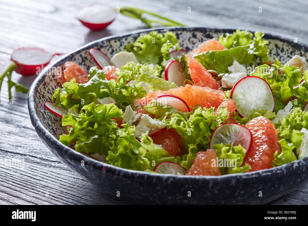 Salade savoureuse avec des ingrédients naturels - laitue, tranches de radis, de morceaux de fromage, grapefuits dans le bol en céramique sur un woo gris Banque D'Images