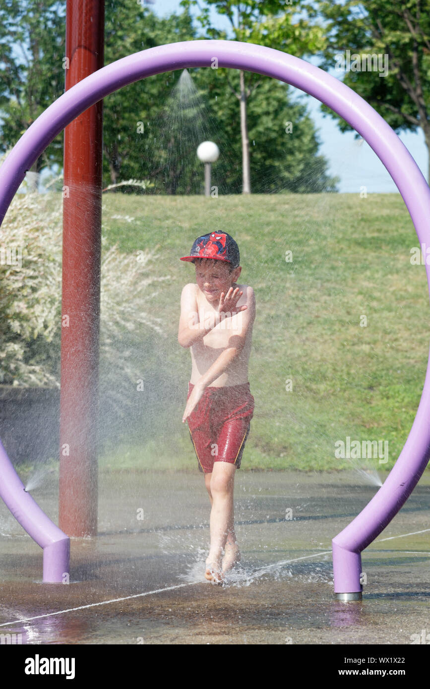 Un jeune garçon (7 ans) grimaces alors qu'il passe par une pulvérisation d'eau dans un parc de l'eau Banque D'Images