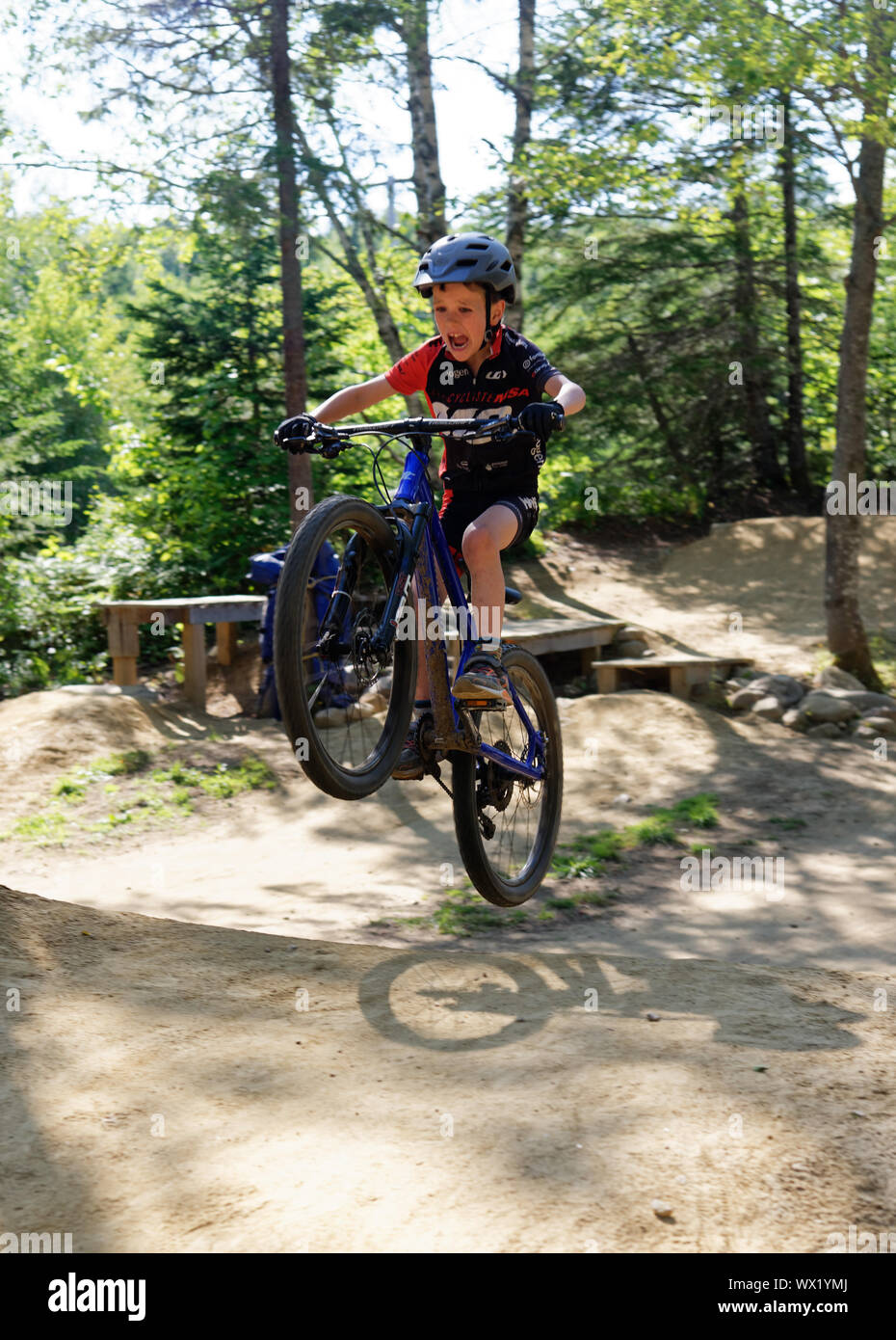 Un garçon de sept ans faire saute sur son vélo de montagne - son visage montrant la concentration et l'effort Banque D'Images