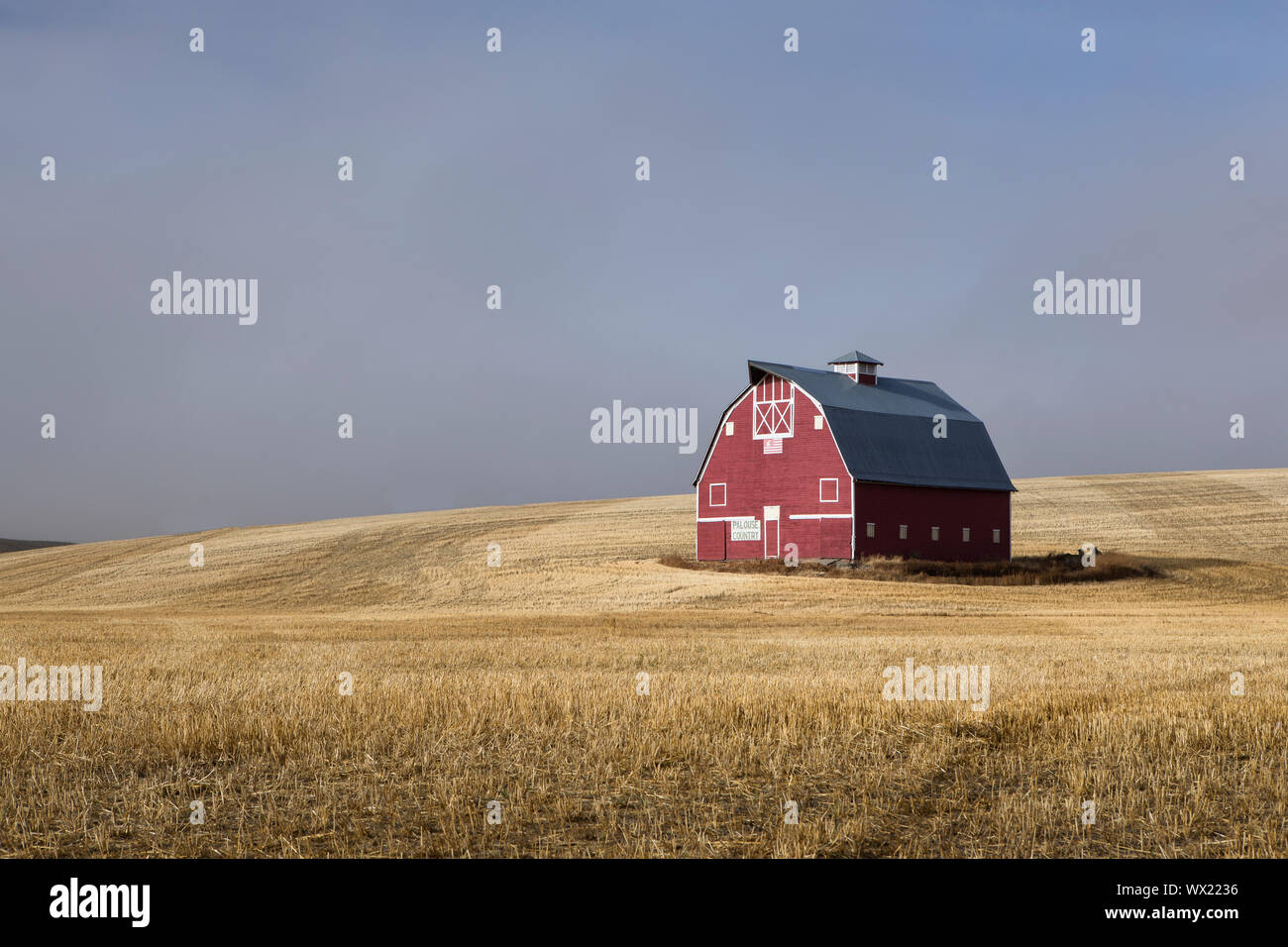 Une grange rouge se trouve dans un champ moissonné avec la levée du brouillard dans l'Est de Washington. Banque D'Images