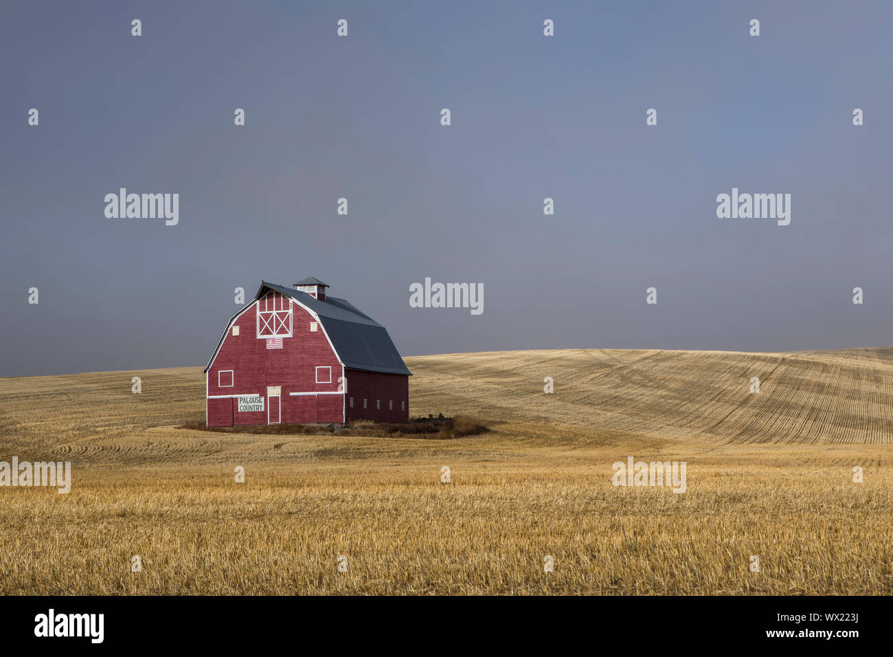 Une grange rouge se trouve dans un champ moissonné avec la levée du brouillard dans l'Est de Washington. Banque D'Images
