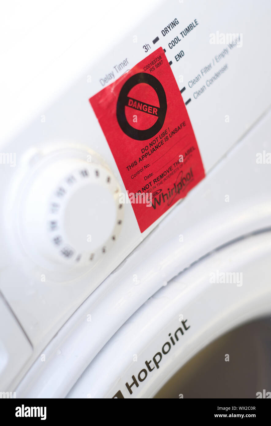 Signe de danger rouge collé sur la face avant d'un sèche-linge Whirlpool Hotpoint blanc Banque D'Images