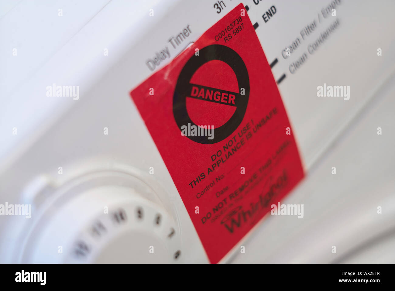 Signe de danger rouge collé sur la face avant d'un sèche-linge Whirlpool Hotpoint blanc Banque D'Images