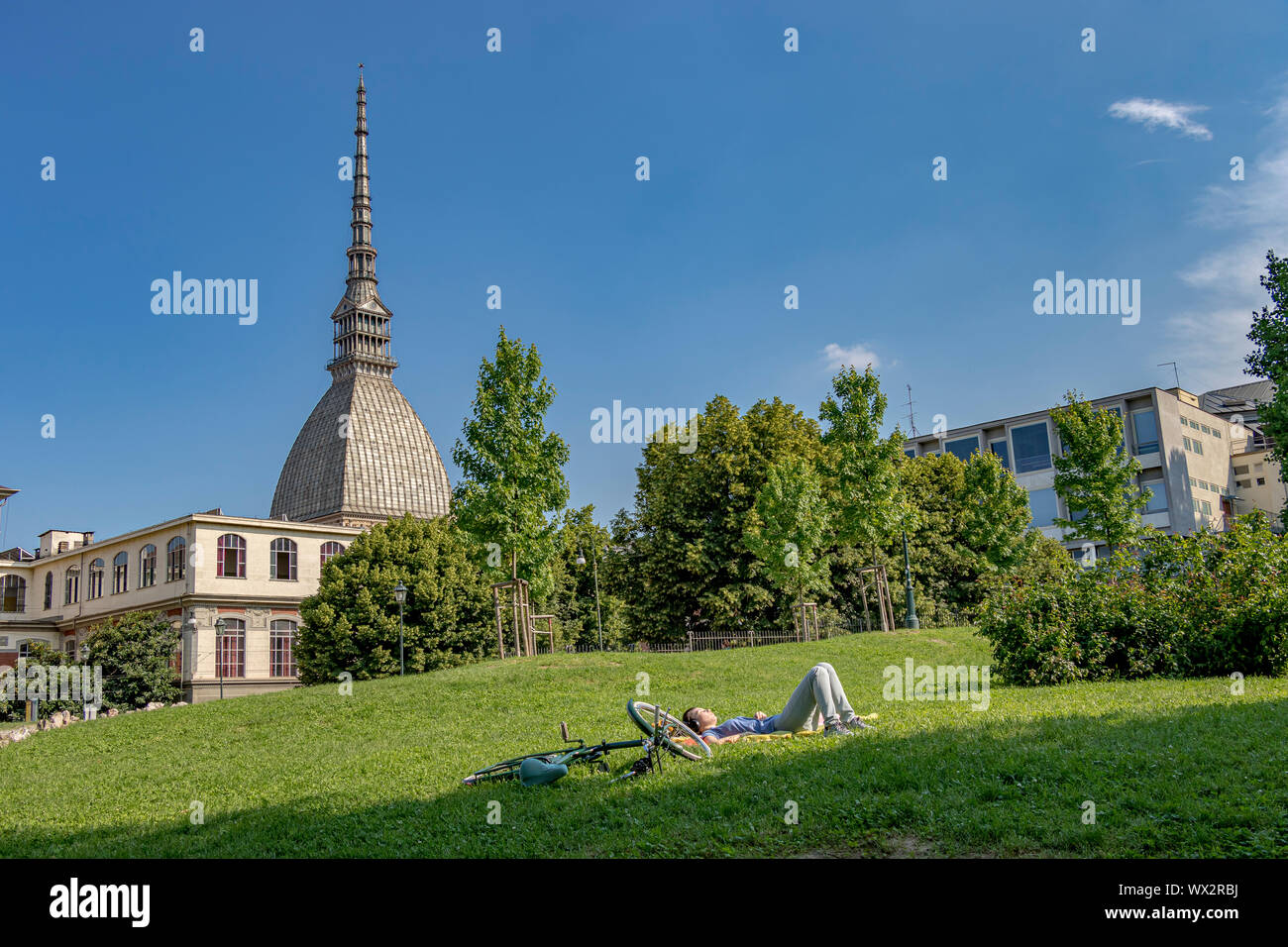 Une personne posée sur l'herbe avec la coupole et la spire de la Mole Antonelliana, en arrière-plan un symbole architectural de la ville de Turin, Italie Banque D'Images