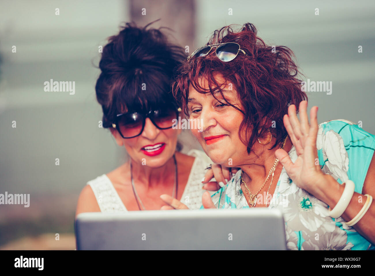 Deux femmes senior - amis en agitant la main et parler tout en ayant un appel vidéo avec leurs amis sur un ordinateur portable dans un café. Banque D'Images