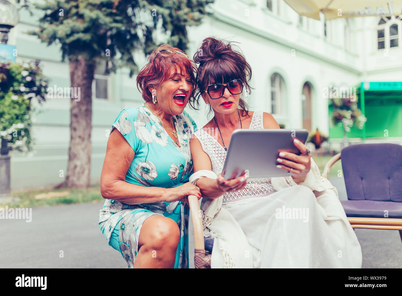 Deux senior women sitting in outdoor cafe en riant et en regardant les médias sociaux et drôles de vidéos virales sur une tablette. Banque D'Images
