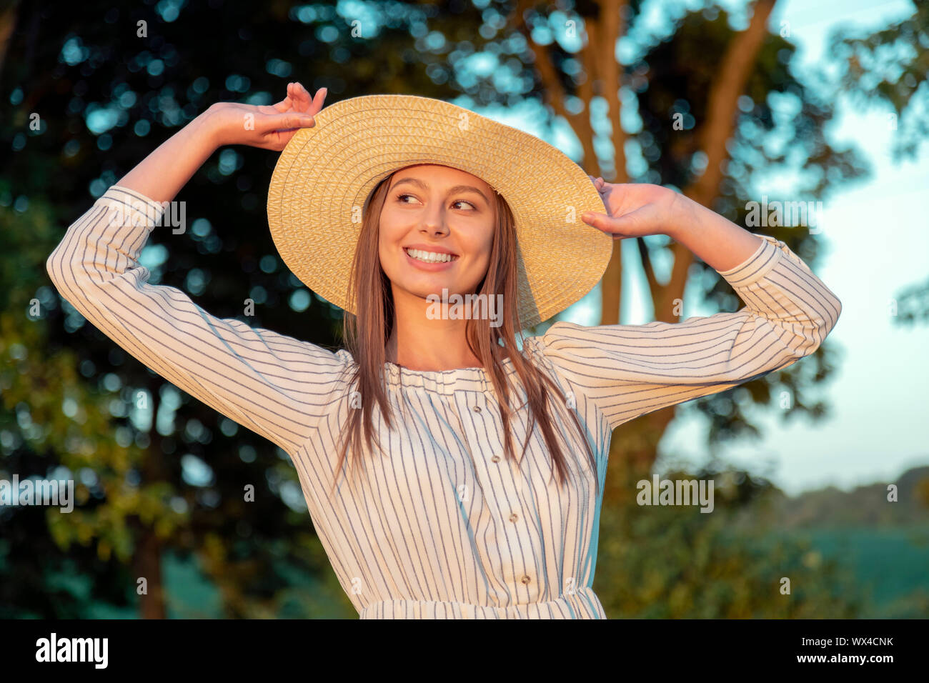 Jolie fille brune posant son chapeau de réglage éclairé par le coucher du soleil d'été soleil Banque D'Images