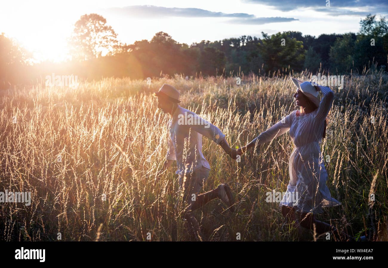 Jeune couple qui traverse un champ éclairé par le coucher du soleil d'été soleil Banque D'Images