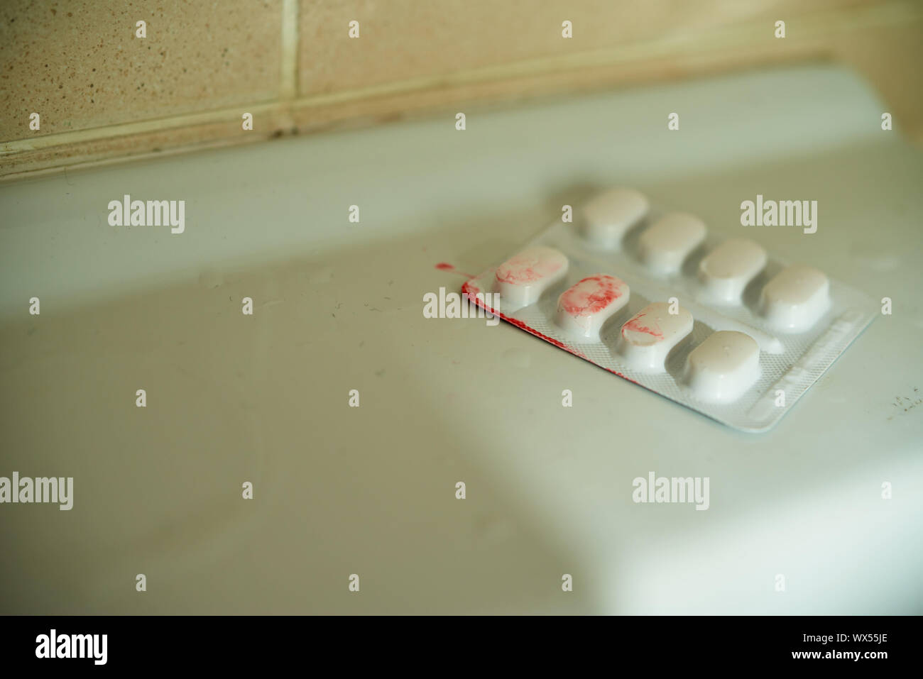 Un paquet de pilules blister blanc sur le côté d'un évier, recouverts d'une substance de type sanguin. Banque D'Images