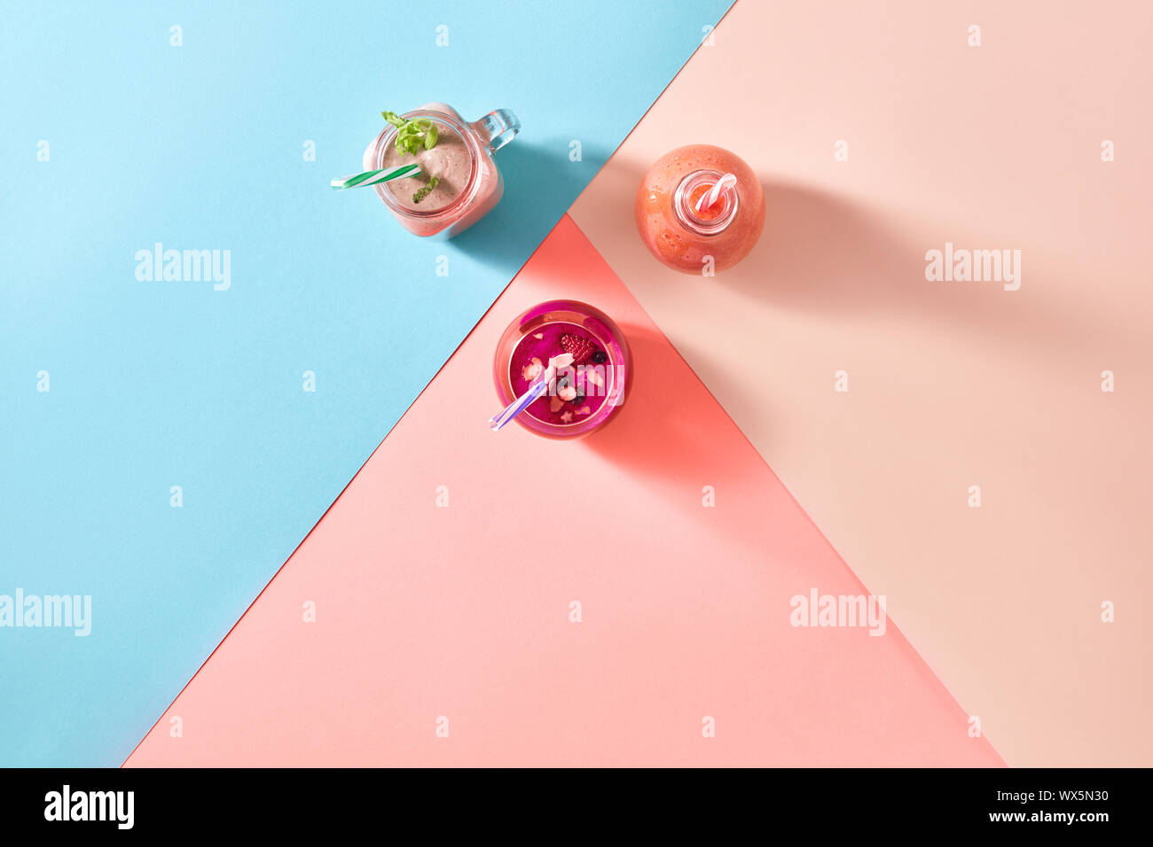 Les matières organiques naturelles accueil smoothies de fruits et légumes dans une bouteille en verre avec des pailles en plastique sur un arrière-plan de la tricolore Banque D'Images