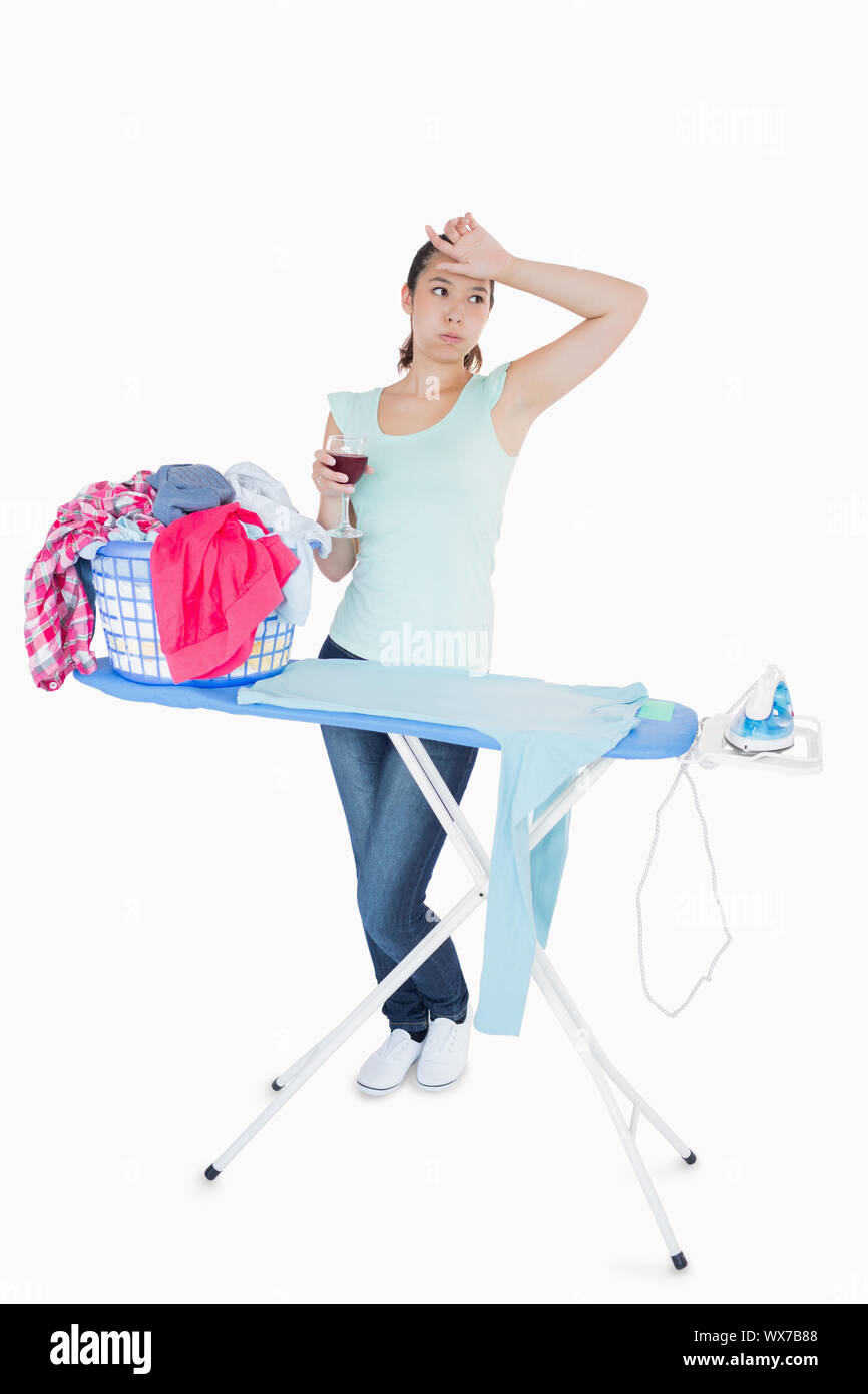 Femme de boire du vin pendant le repassage d'un panier de blanchisserie Banque D'Images