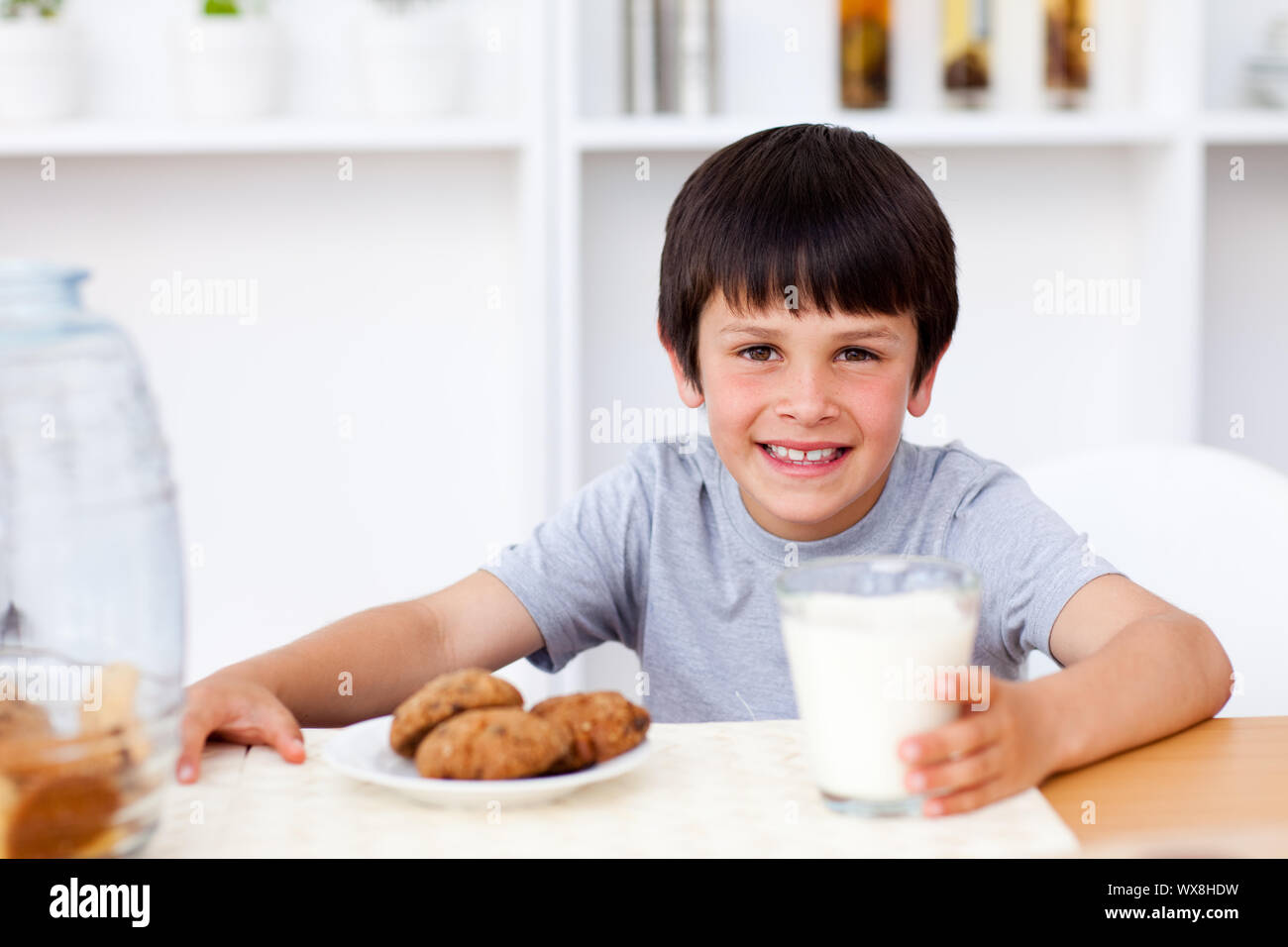 Happy boy manger des biscuits et boire du lait dans la cuisine Banque D'Images