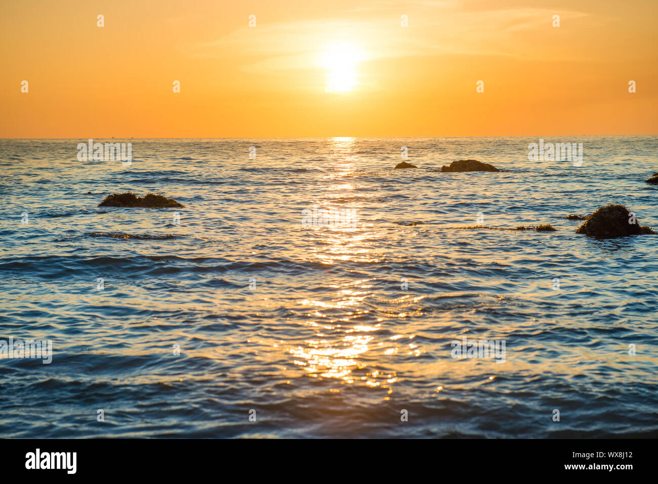 Paysage au coucher du soleil avec la plage, le soleil et des pierres sur mer  Photo Stock - Alamy