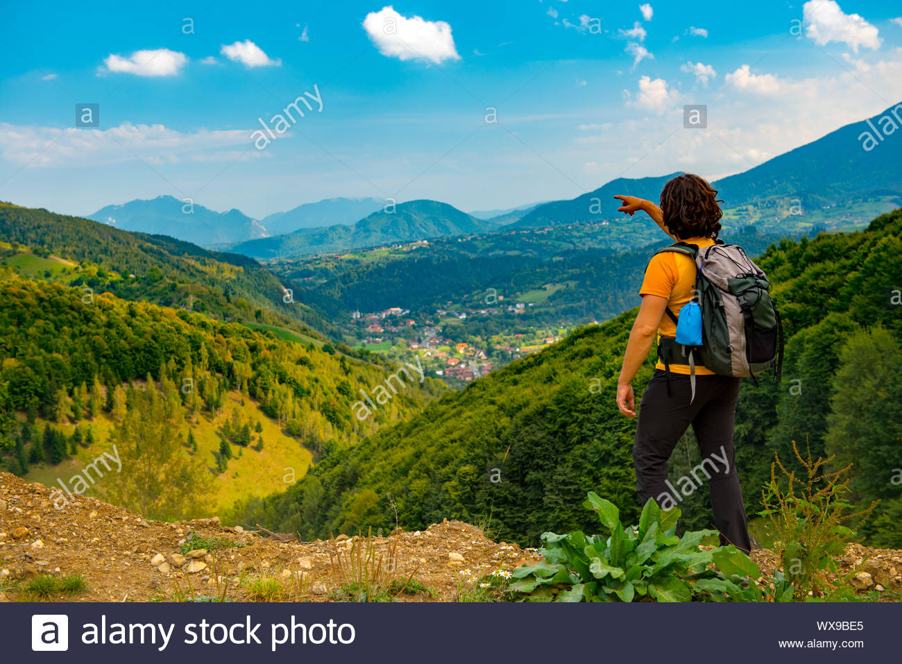 Jeune randonneur pointant vers un beau paysage de montagnes couvertes de forêts. Randonnée dans un beau jour d'été. Banque D'Images