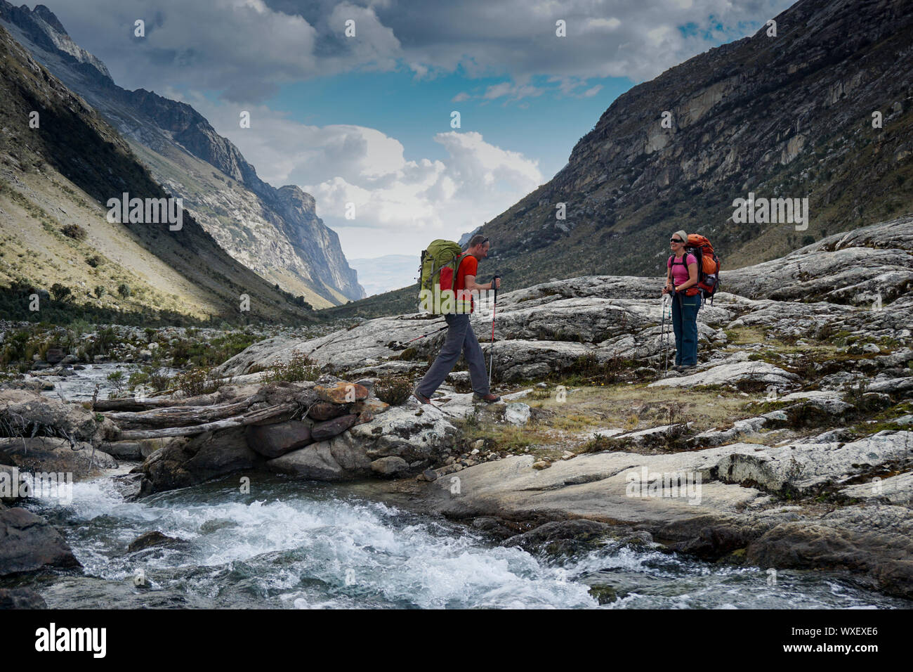 L'homme et la femme dans le backpacker Andes du Pérou traverser un ruisseau de montagne sauvages Banque D'Images