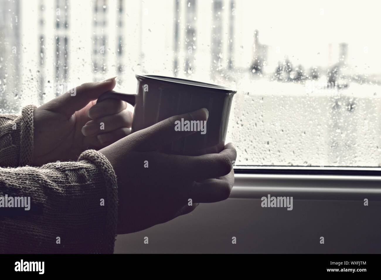 Main tenant tasse de café chaud ou un thé dans la lumière du soleil du matin sur un fond de fenêtre humide avec des gouttes de confort / Pause café Banque D'Images