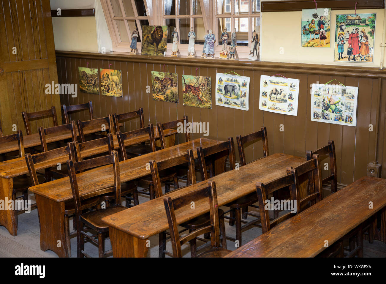UK, County Durham, Beamish Museum, fosse, Village, École classe junior vers 1913, d'un bureau et de chaises ci-dessous ediucational matériel sur mur Banque D'Images