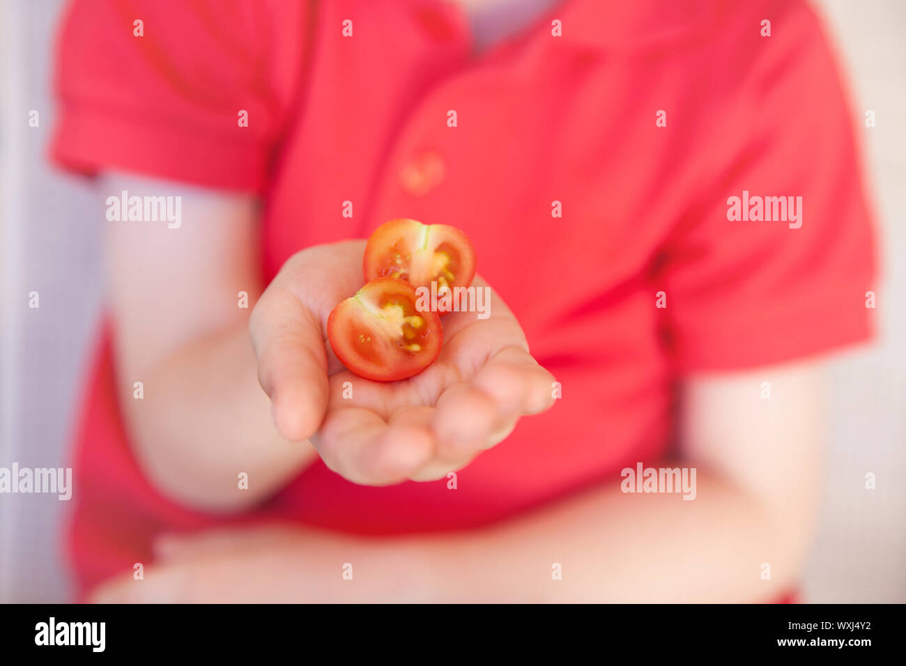 Garçon tenant une moitié de tomate cerise Banque D'Images