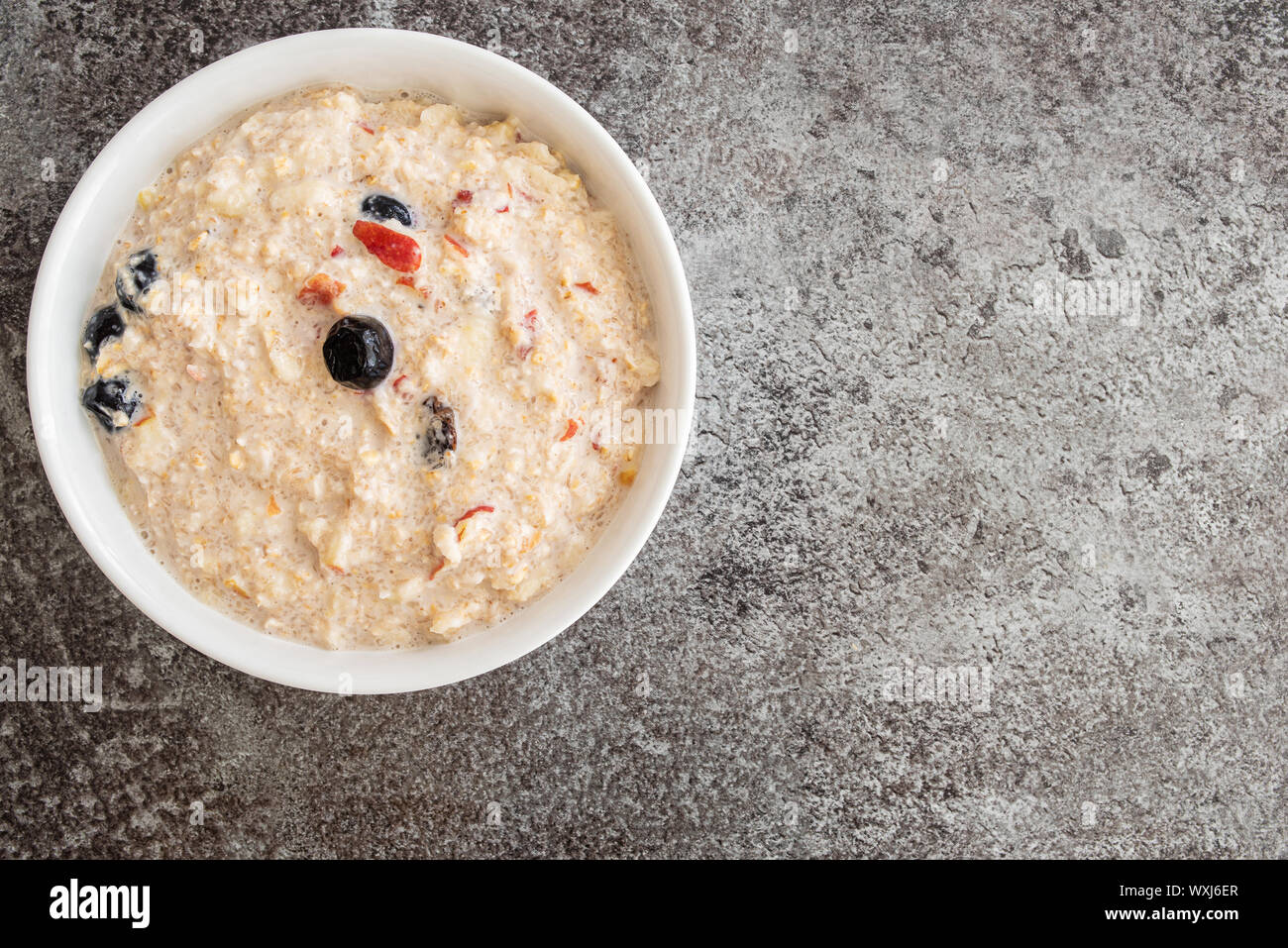 Vue de dessus du bol de céréales rempli de Bircher muesli avec les bleuets et les canneberges sur le comptoir de cuisine en pierre Banque D'Images Vue de dessus du bol de céréales rempli de Bircher muesli avec les bleuets et les canneberges sur le comptoir de cuisine en pierre Banque D'Images