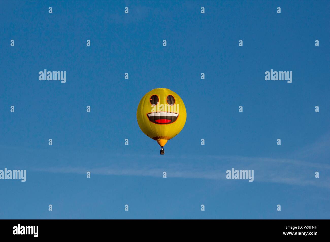 Un heureux jaune montgolfière emoji voler contre un ciel bleu. Smiley Banque D'Images