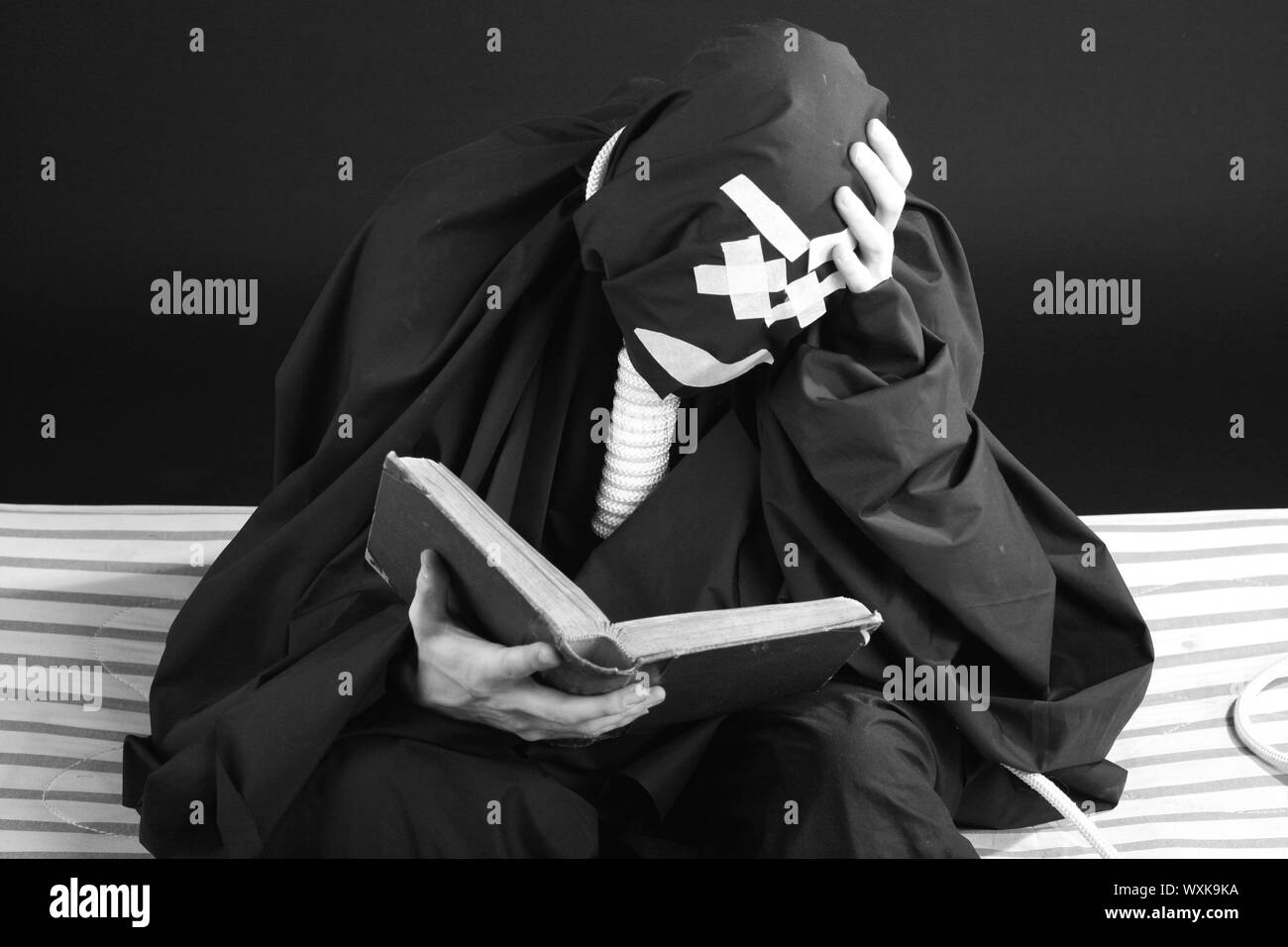 Mime noir avec une corde sur le cou sur fond noir reading book Banque D'Images
