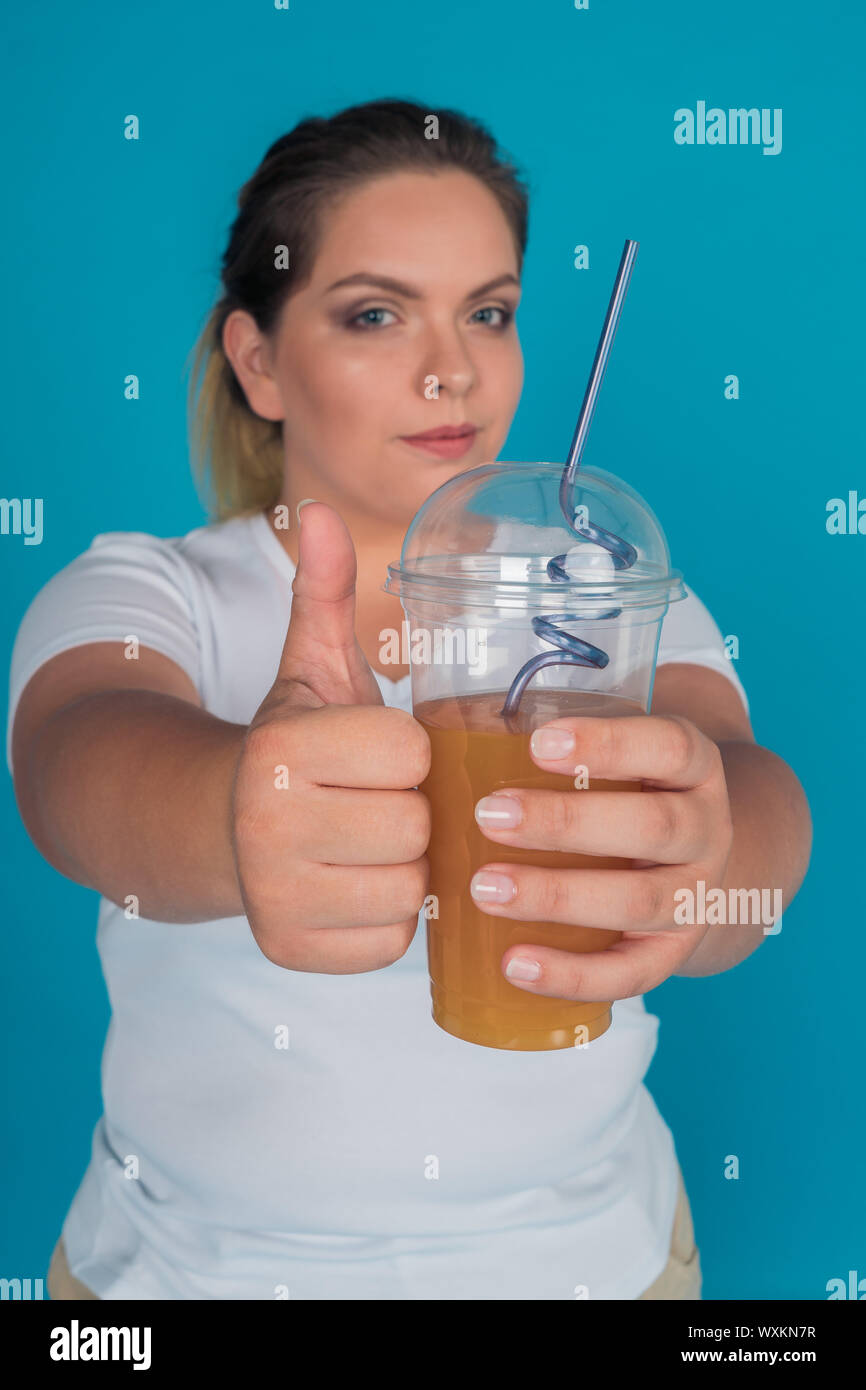 Chubby girl détient un smoothie sain dans sa main et tient son pouce levé. La notion de perte de poids grâce à un régime alimentaire sain. Banque D'Images