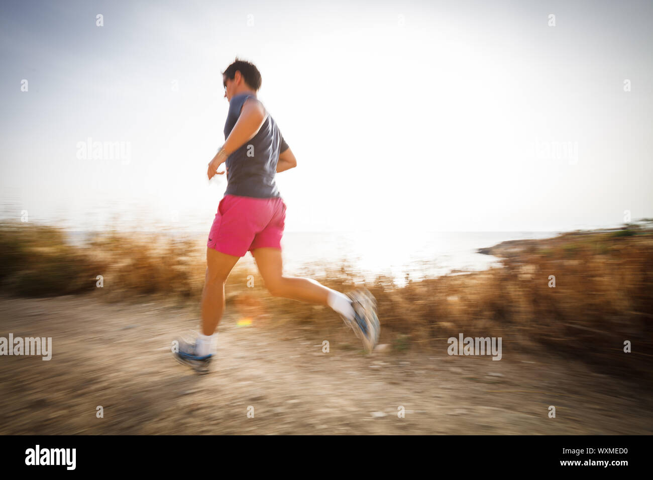 Jeune homme de race blanche s'exécutant sur un chemin mi-ombre sur un beau soir d'été, la formation pour le marathon (motion image floue) Banque D'Images