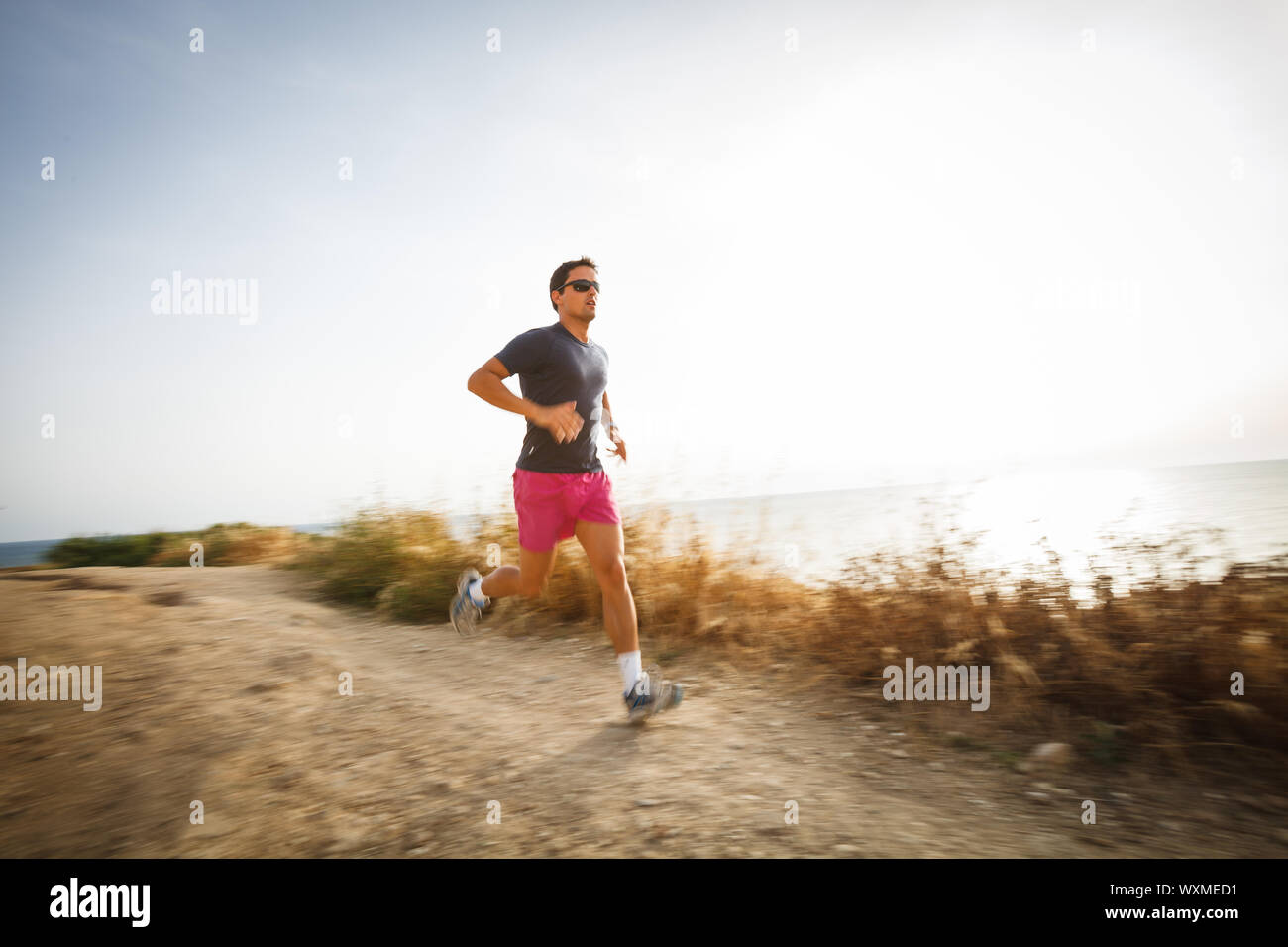 Jeune homme de race blanche s'exécutant sur un chemin mi-ombre sur un beau soir d'été, la formation pour le marathon (motion image floue) Banque D'Images