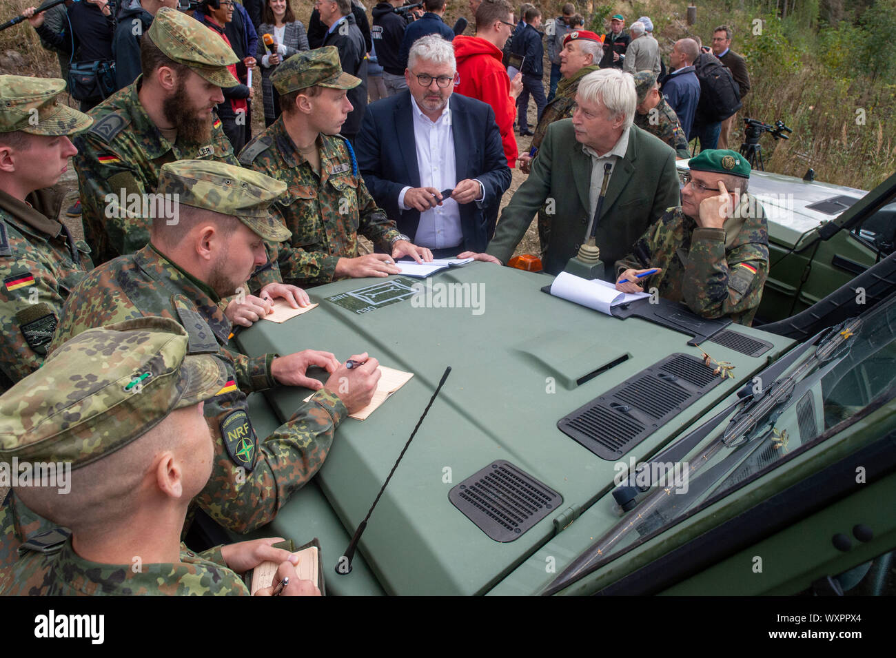 16 septembre 2019, la Saxe-Anhalt, Straßberg : Les soldats du bataillon logistique de 171 de Burg et 172 du bataillon logistique de Beelitz stand avec Lutz-Georg Berkling (l) du ministère de l'intérieur de la Saxe-Anhalt, Egbert Thile (M), chef de l'Office des forêts du Harz et du Lieutenant-colonel Bertram Schuster, Coordonnatrice des opérations du Commandement à l'état de Saxe-anhalt le capot d'un véhicule hors route des forces armées allemandes et discuter d'autres actions communes dans la semaine à venir. Les soldats sont les premiers enquêteurs des forces armées allemandes à se renseigner sur leur prochaine depl Banque D'Images