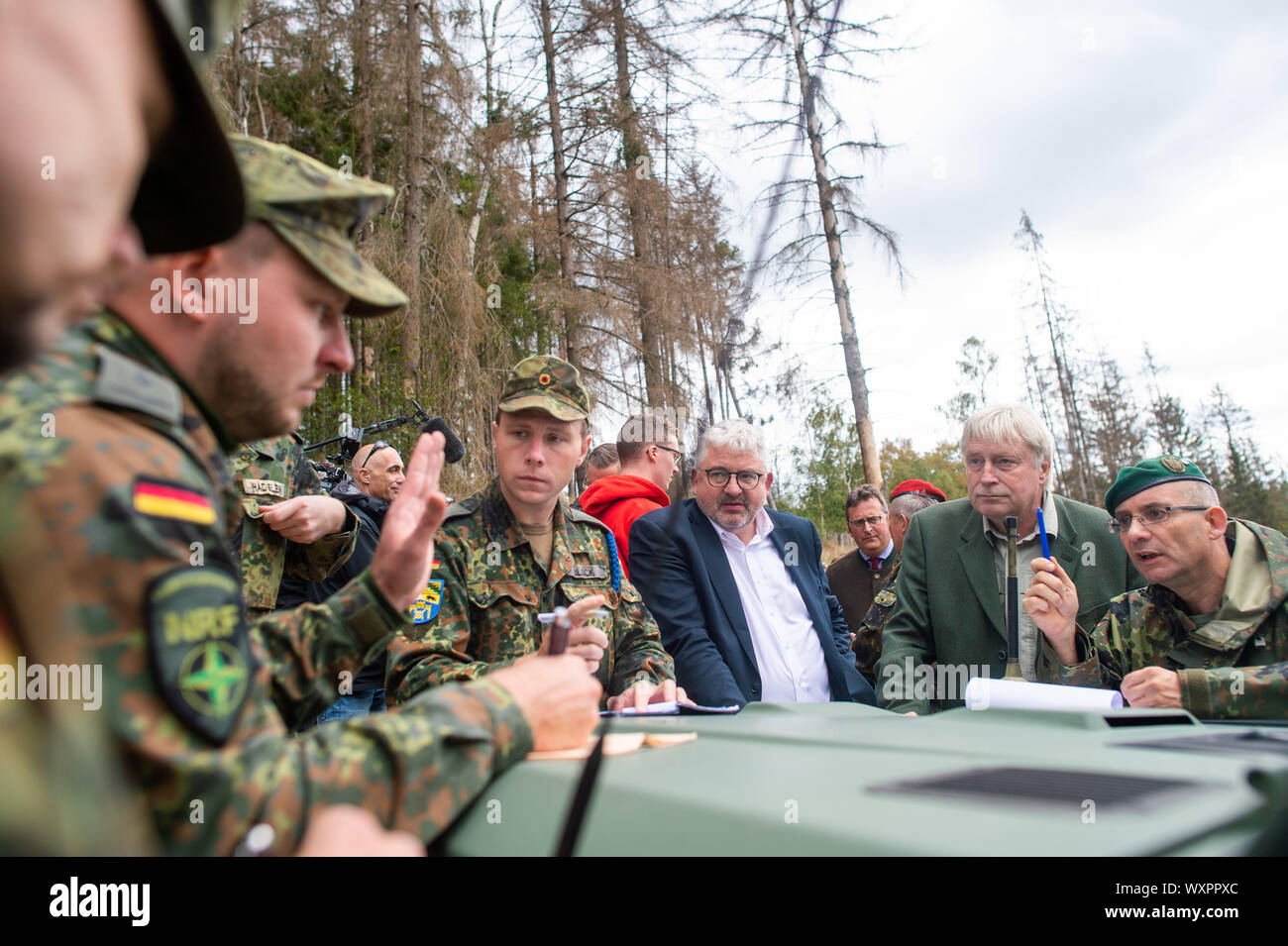 17 septembre 2019, la Saxe-Anhalt, Straßberg : Les soldats du bataillon logistique de 171 de Burg et 172 du bataillon logistique de Beelitz stand avec Lutz-Georg Berkling (l.) du ministère de l'intérieur de la Saxe-Anhalt, Egbert Thile (m.), chef de l'Office des forêts du Harz et du Lieutenant-colonel Bertram Schuster, Coordonnatrice des opérations du Commandement à l'état de Saxe-anhalt le capot d'un véhicule hors route des forces armées allemandes et discuter d'autres actions communes dans la semaine à venir. Les soldats sont les premiers enquêteurs des forces armées allemandes à se renseigner sur leur prochaine de Banque D'Images