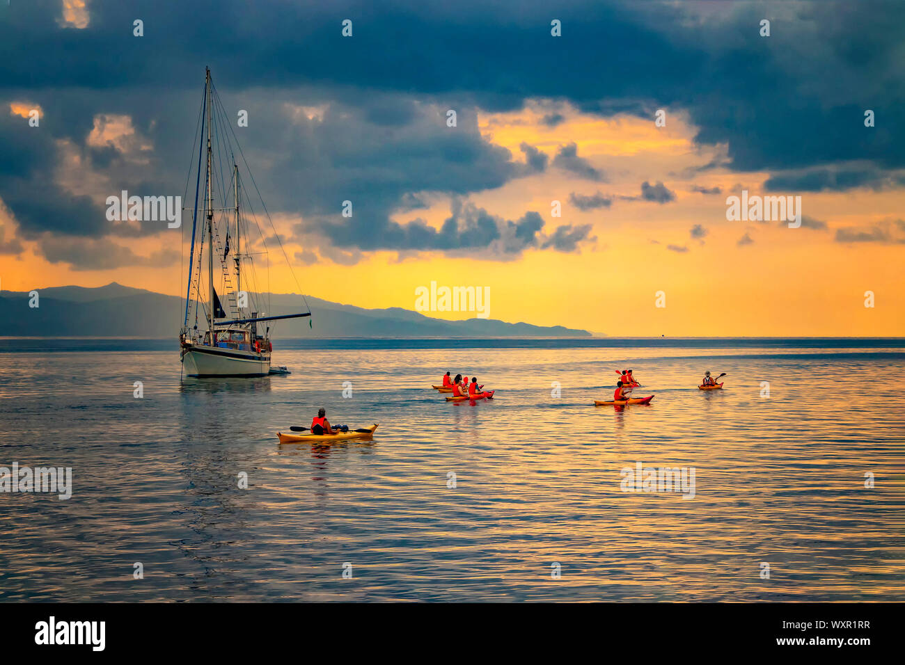 Location dans la mer Méditerranée à l'aube, Cagliari, Italie. Les gens de la voile sur les kayaks sur la mer sous le soleil. Le soleil illumine l'île avec Banque D'Images