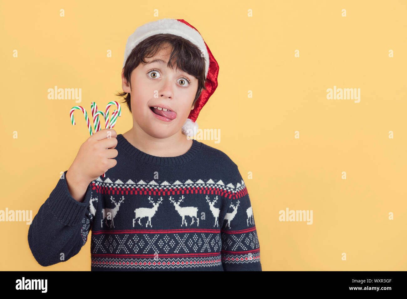 Child Wearing Christmas Santa Claus Hat et des cannes de bonbon sur fond jaune Banque D'Images