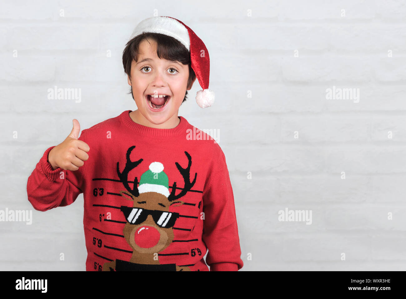 Smiling child Wearing Christmas Santa Claus Hat showing thumb up sur fond brique Banque D'Images
