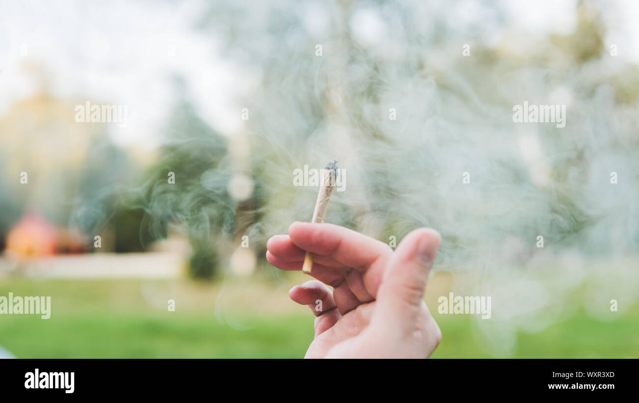 Le jeune fumeur de marijuana médicale à l'extérieur. conjointe Le jeune homme fumer du cannabis blunt, close-up. Le cannabis est un concept de médecine de fines herbes. Banque D'Images
