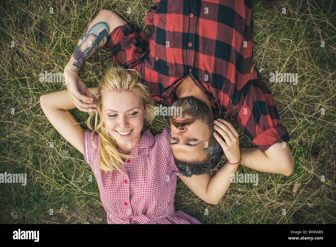 Jeune couple dans l'amour. Deux personnes, blonde et barbu, allongé sur l'herbe verte. Petite amie et petit ami de jouer les uns avec les autres cheveux. Banque D'Images