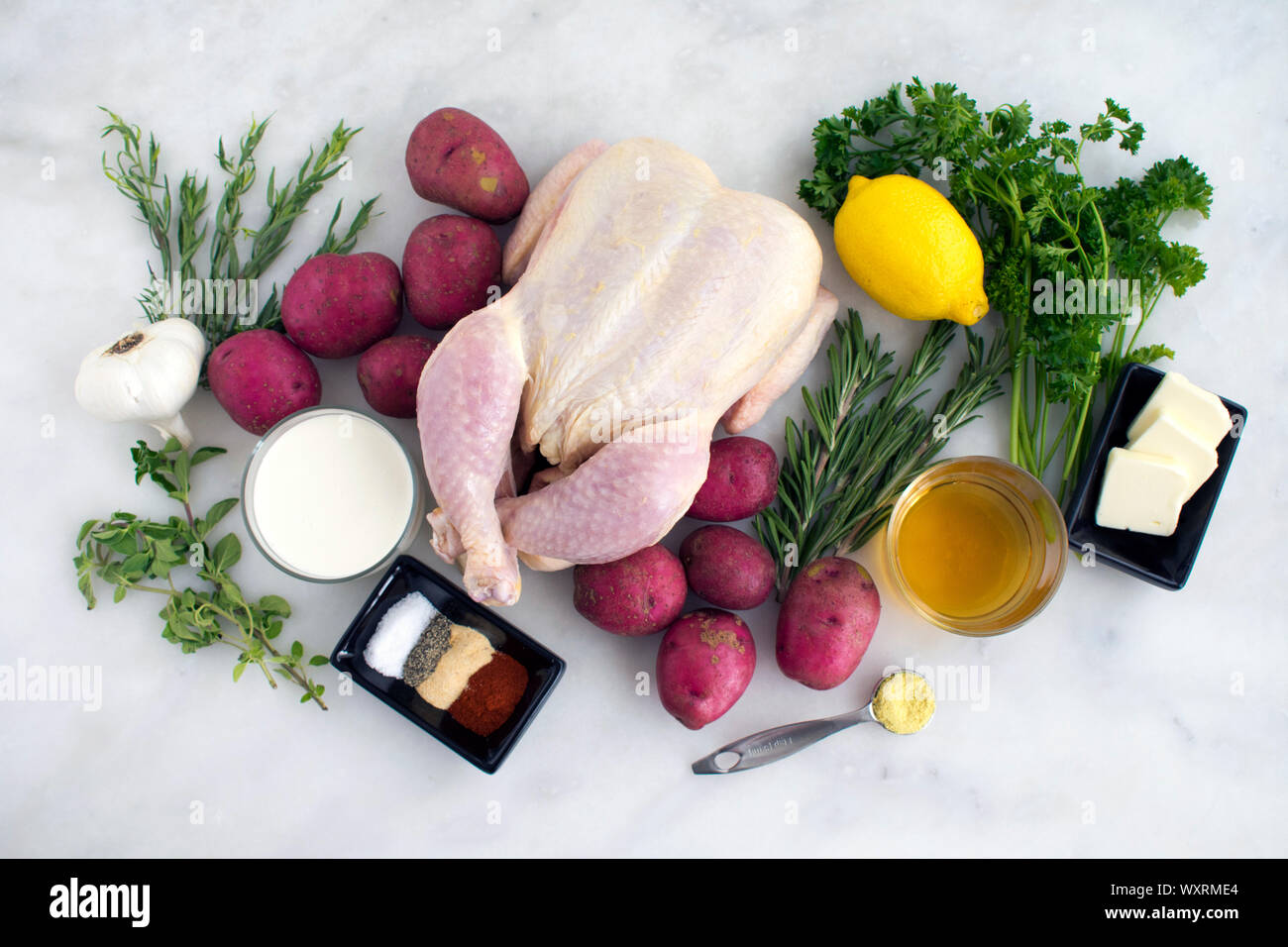 Pot d'herbe et crémeuse au citron Ingrédients : Poulet rôti un poulet cru entier, bébé pommes de terre rouges, des herbes fraîches, et d'autres ingrédients sur le marbre blanc Banque D'Images