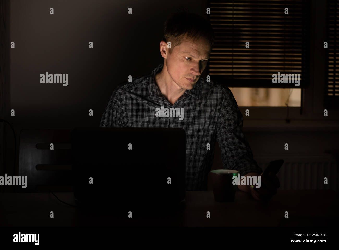 L'homme au travail dans la nuit est à la recherche dans un écran du smartphone. Banque D'Images