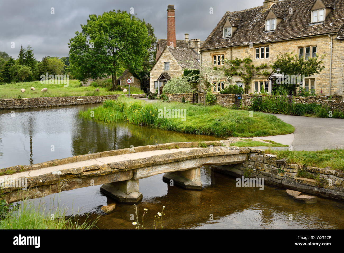 Cotswold jaune passerelle de calcaire sur la rivière Eye à Lower Slaughter village de Cheltenham en Angleterre avec les bâtiments du musée du Vieux Moulin Banque D'Images