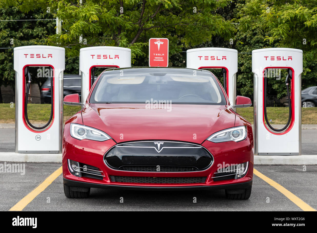 Avant du modèle Tesla S en stationnement à la station de Supercharger Tesla avec une route très fréquentée derrière. Banque D'Images