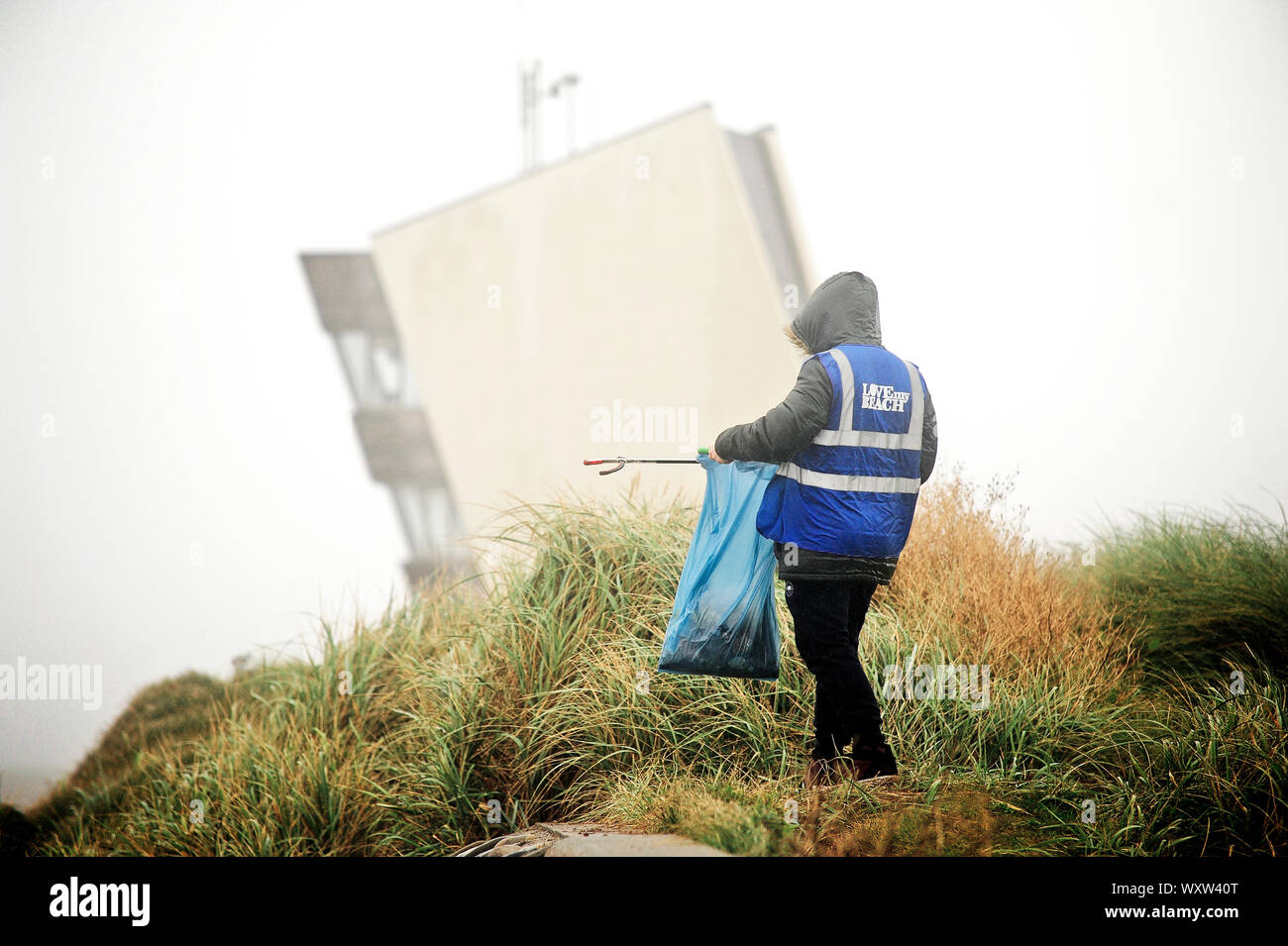 Picker solitaire de litière travaillant devant la tour d'observation de Rossall point sur le front de mer de Fleetwood par temps humide et froid Banque D'Images