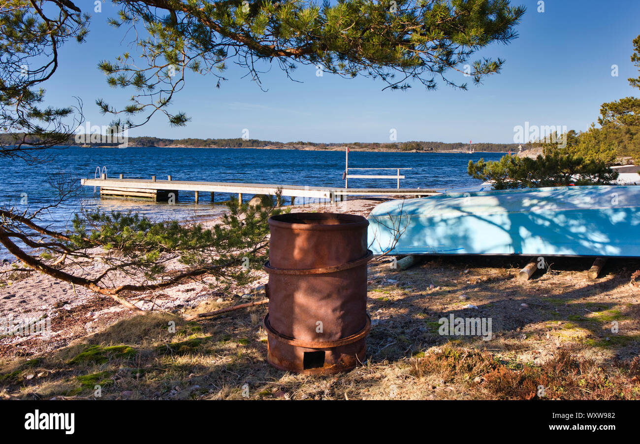 Baril rouillé, retroussé bleu bateau et jetée en bois rustique sur la côte de la mer Baltique, Sandhamn, archipel de Stockholm, Suède Banque D'Images