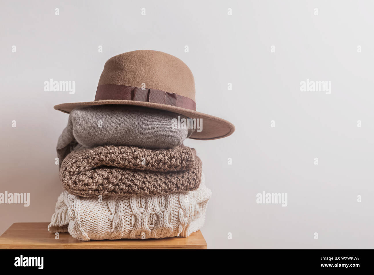 Pile d'hiver en laine tricoté chaud chapeau de feutre et sweates sur le tabouret en bois près du mur blanc Banque D'Images