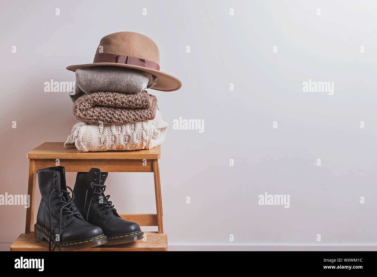 Automne ou hiver armoire. Pile de pulls chauds pliée, chapeau de feutre et des bottes sur le petit banc de bois dans la chambre avec des murs blancs Banque D'Images