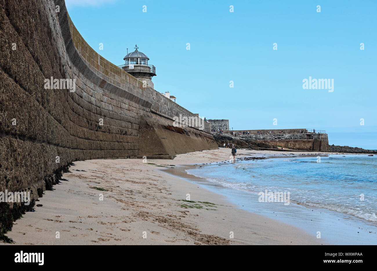 Le redoutable mur de Smeaton's Pier à St Ives vu du dessous à marée basse, avec une figure solitaire marchant le long de la plage Banque D'Images