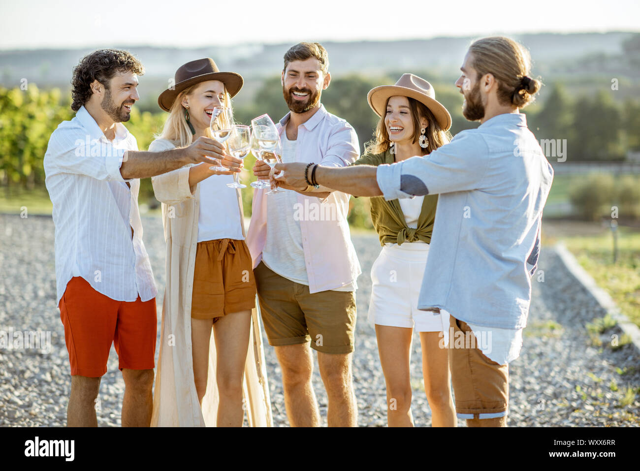 Groupe de jeunes amis habillés de désinvolture à traîner ensemble, dégustation de vin et de la vigne sur clinking glasses on a sunny day Banque D'Images