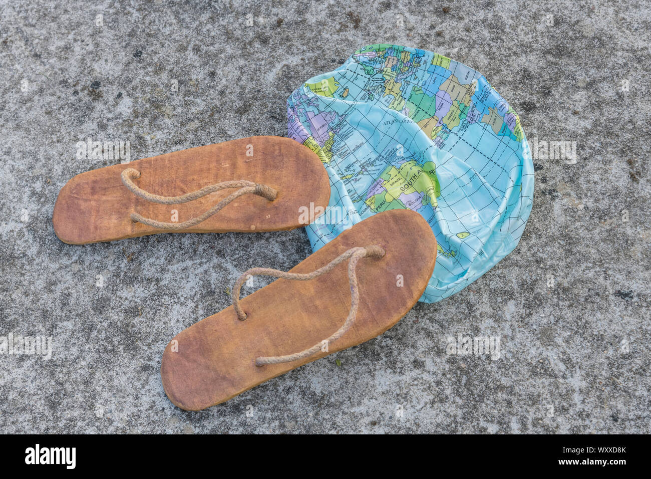 Hippy usés tongs & globe dégonflé sur surface en béton. Métaphore 250-504, télévision earthers, théories du complot, preuve de la terre plate, la pseudoscience Banque D'Images