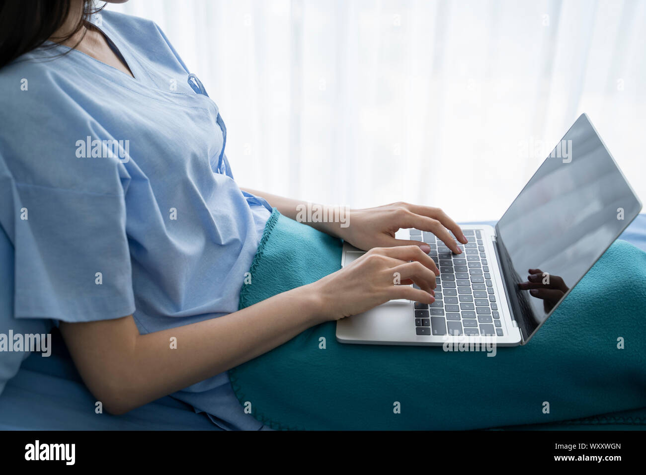 Young Asian woman malade couché dans un lit d'hôpital à l'aide d'un ordinateur portable pour se détendre lorsqu'elle un dédommagement pour les malades à l'hôpital. Banque D'Images