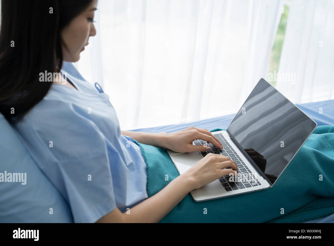 Young Asian woman malade couché dans un lit d'hôpital à l'aide d'un ordinateur portable pour se détendre lorsqu'elle un dédommagement pour les malades à l'hôpital. Banque D'Images